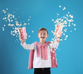 Cute boy scattering popcorn from buckets on color background