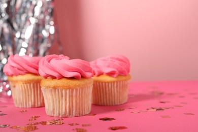 Photo of Delicious cupcakes with bright cream and confetti on pink background, space for text