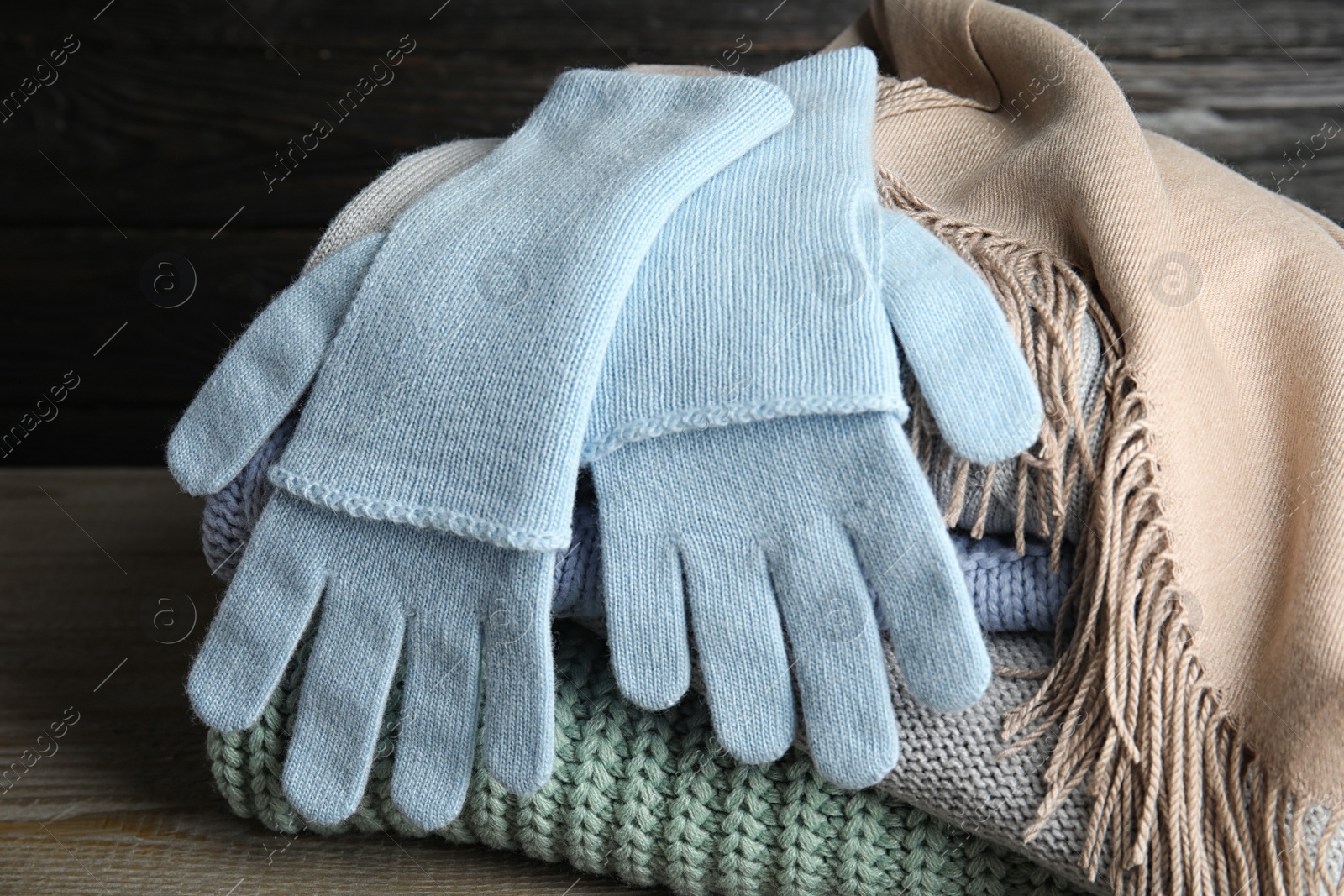 Photo of Stacked sweaters and gloves on wooden table, closeup. Autumn clothes