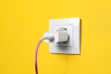 Photo of Charger adapter plugged into power socket on yellow wall, closeup. Electrical supply