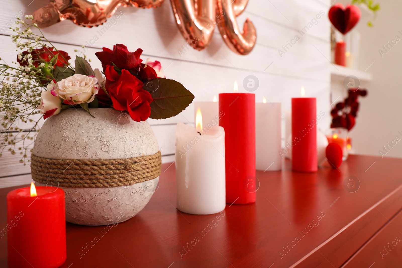 Photo of Burning candles and vase with flowers on red table indoors. Valentine's Day celebration