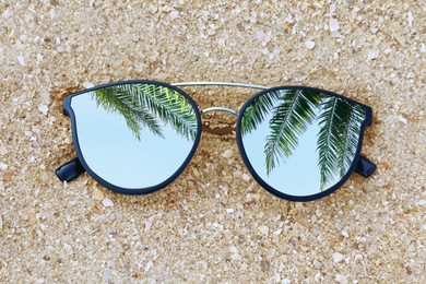 Image of Green palm leaves mirroring in sunglasses on sandy beach, top view