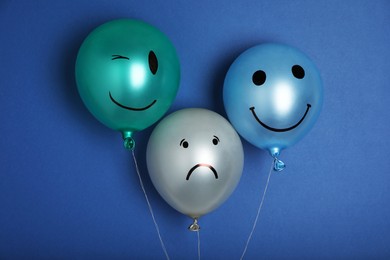 Photo of Balloon with sad face among happy ones on blue background. Depression concept