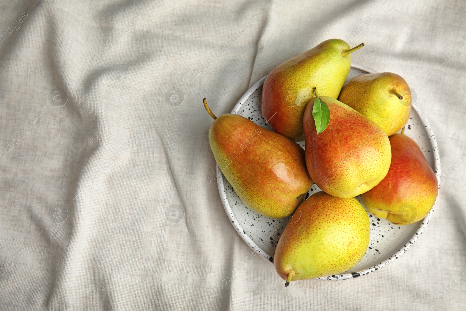 Photo of Plate with ripe juicy pears on light fabric, top view. Space for text