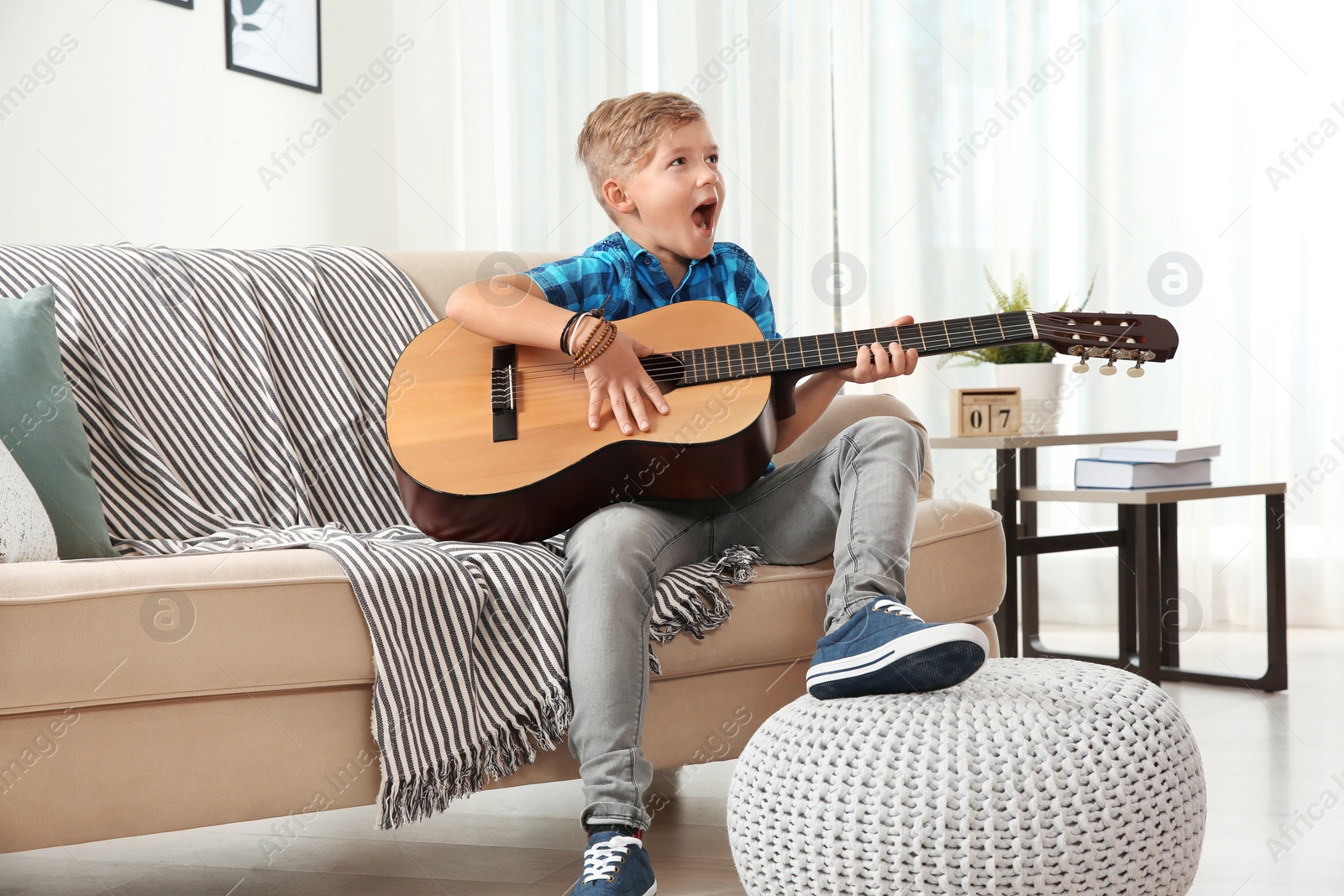 Photo of Cute little boy playing guitar on sofa in room