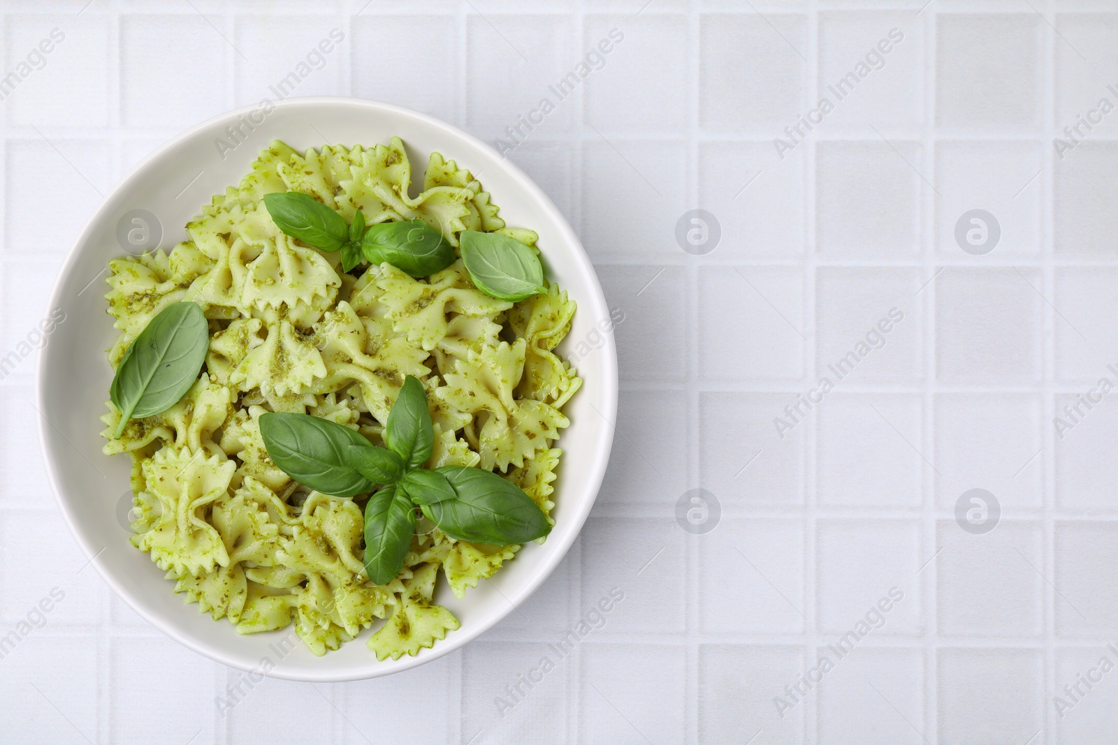 Photo of Delicious pasta with pesto sauce and basil on white tiled table, top view. Space for text