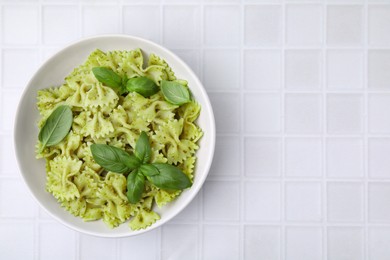 Delicious pasta with pesto sauce and basil on white tiled table, top view. Space for text