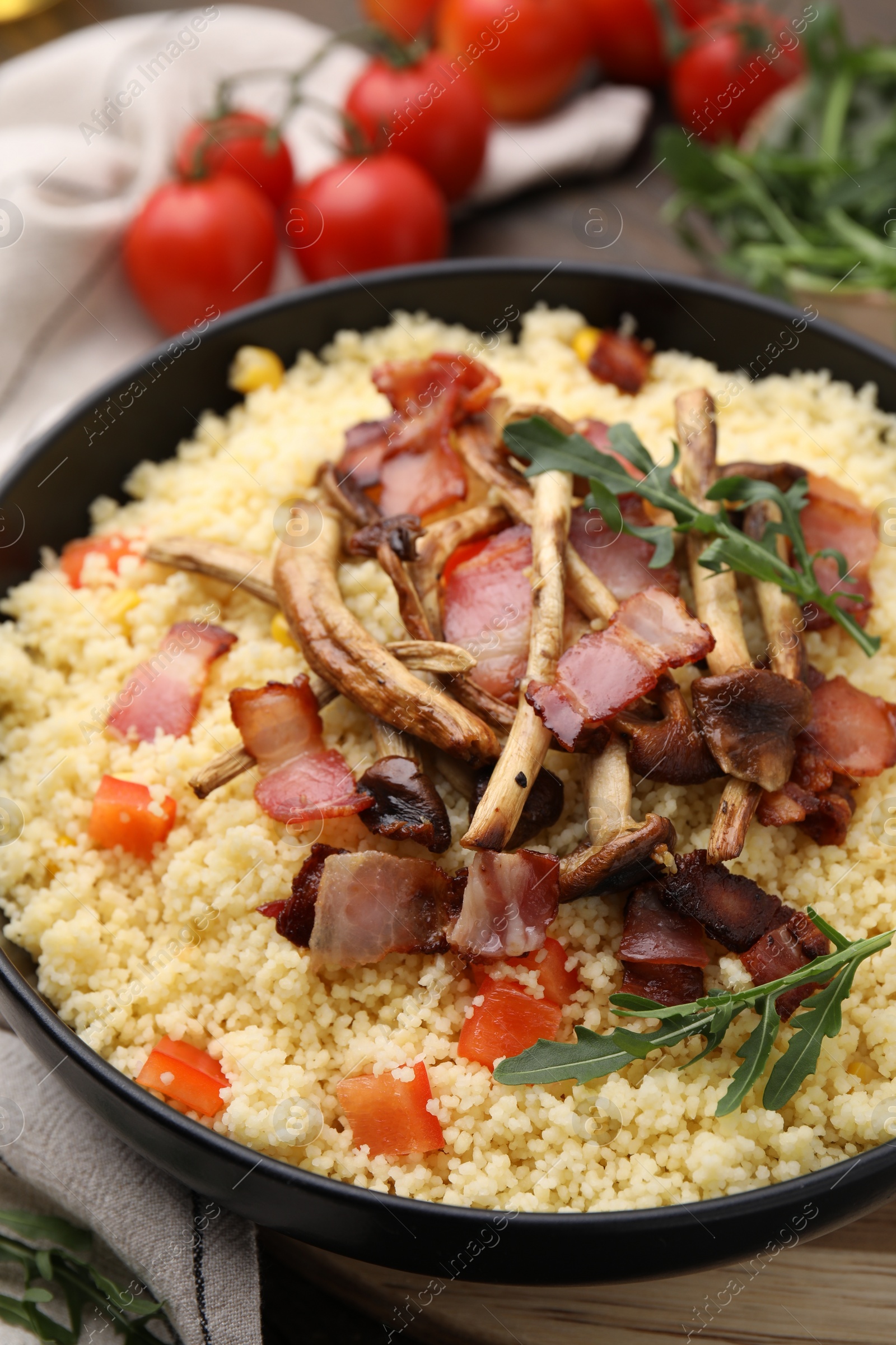 Photo of Tasty couscous with mushrooms and bacon in bowl on table, closeup