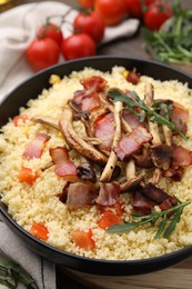 Tasty couscous with mushrooms and bacon in bowl on table, closeup