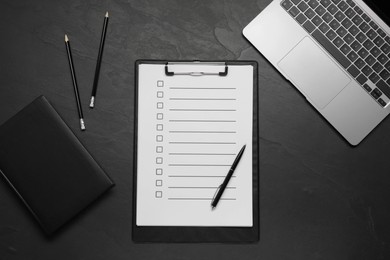 Photo of Clipboard with checkboxes, pen and laptop on black table, flat lay