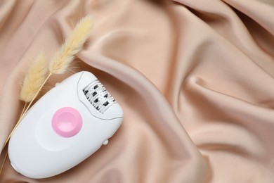 Photo of Modern epilator and fluffy dry plants on silk fabric, top view. Space for text