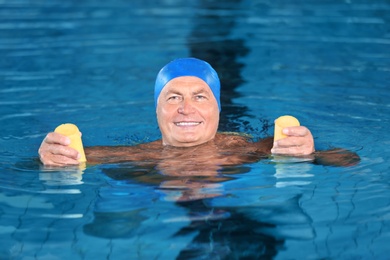 Photo of Sportive senior man doing exercises in indoor swimming pool