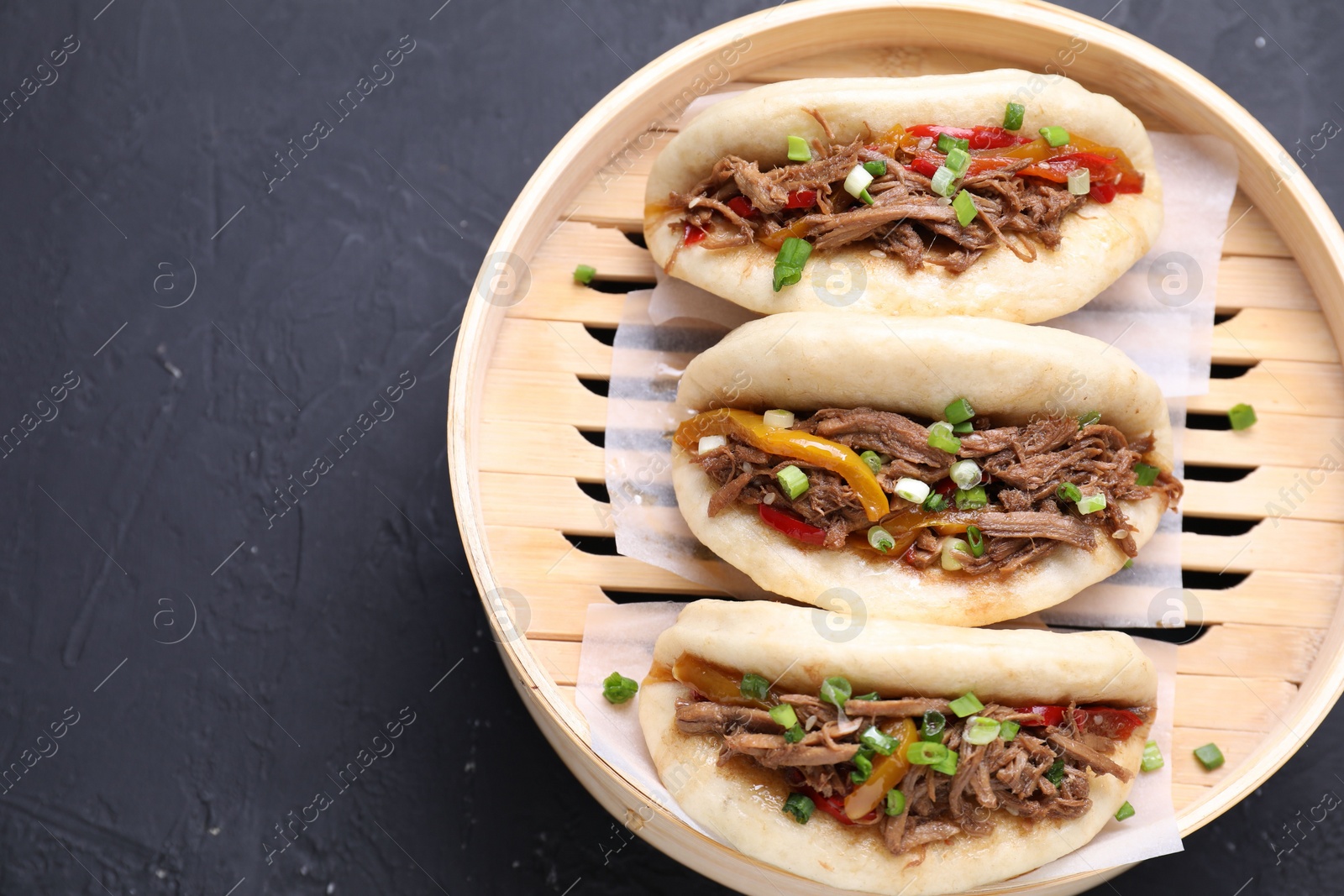 Photo of Delicious gua bao in bamboo steamer on black table, top view. Space for text