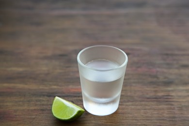 Photo of Mexican tequila shot with lime slice on wooden table, closeup and space for text. Drink made from agave