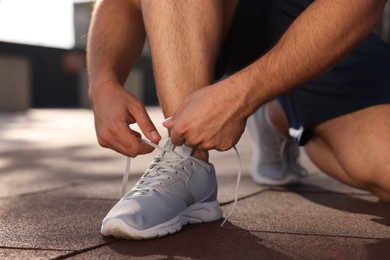 Photo of Man tying shoelaces before running outdoors on sunny day, closeup