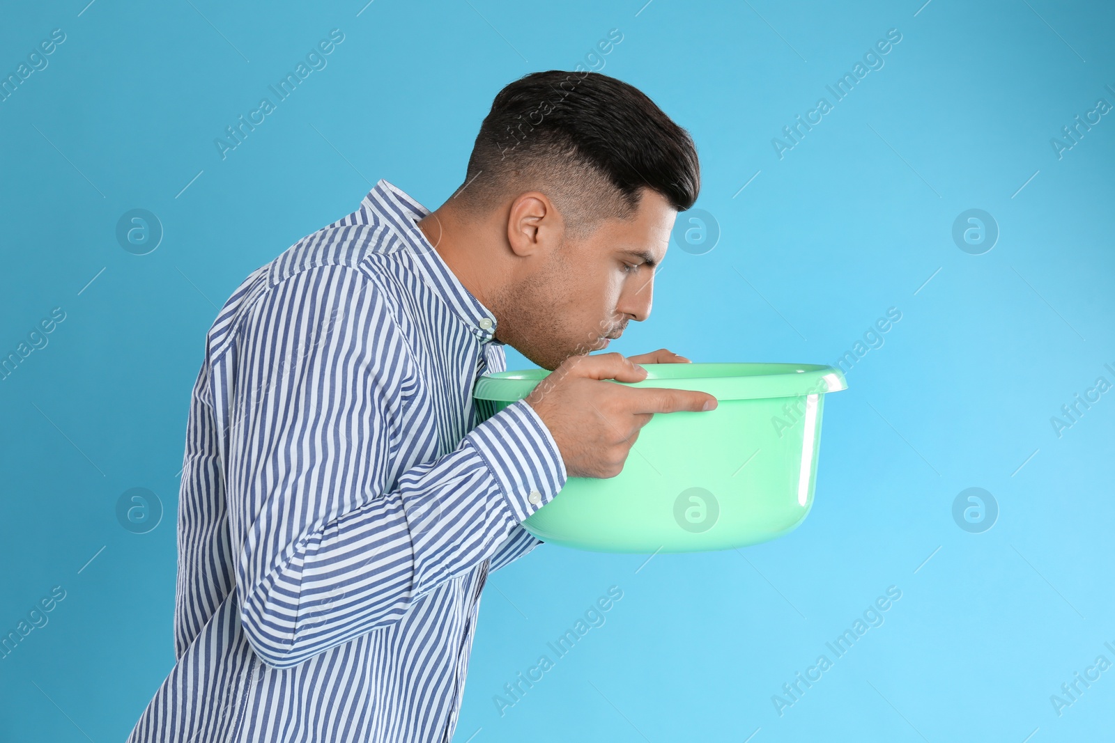 Photo of Man with basin suffering from nausea on light blue background. Food poisoning