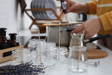 Photo of Woman making aromatic candles at white table indoors, focus on empty jars