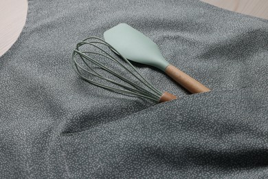 Photo of Stylish apron, spatula and whisk on table, closeup