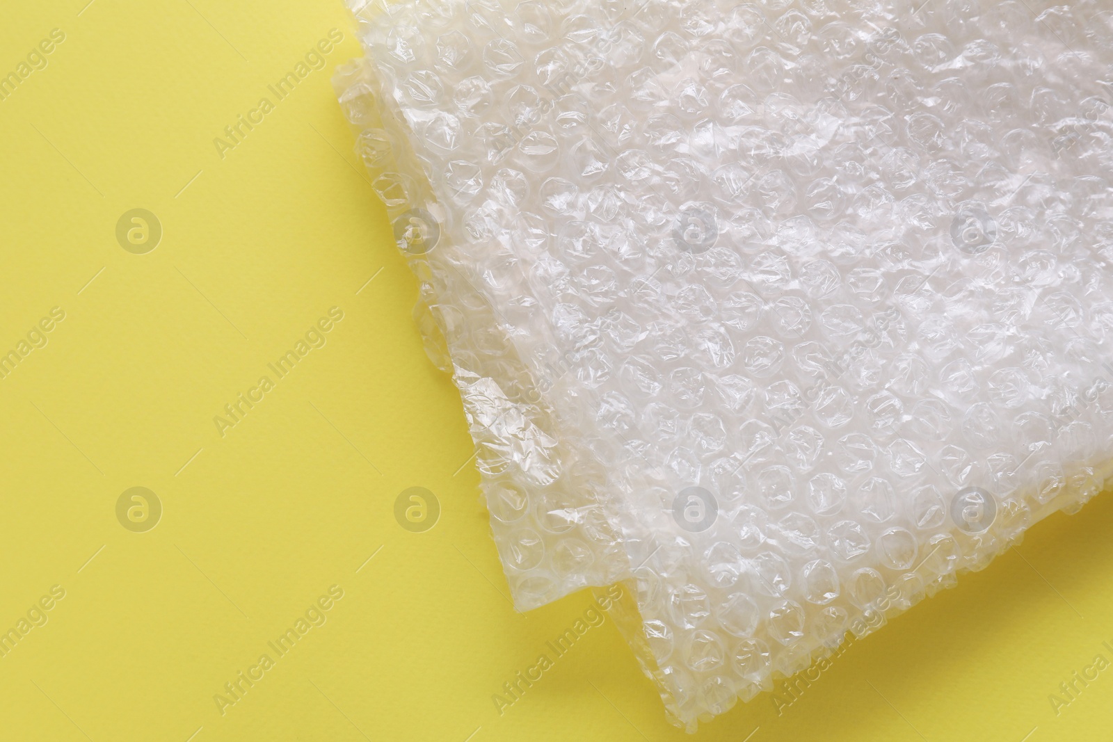 Photo of Transparent bubble wrap on yellow background, top view. Space for text