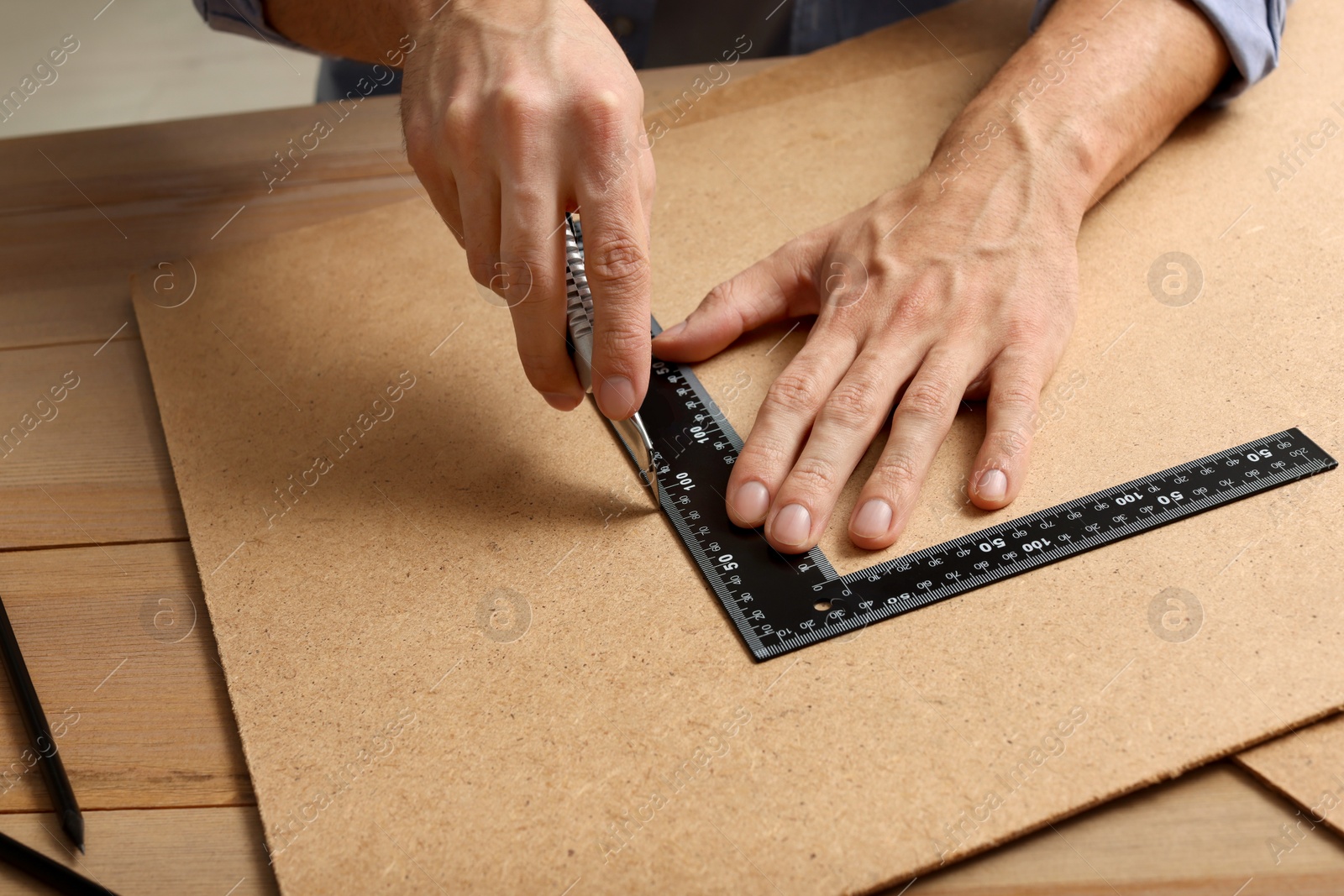 Photo of Man cutting chip board with utility knife and ruler at table, closeup