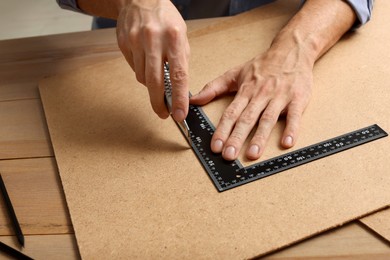 Photo of Man cutting chip board with utility knife and ruler at table, closeup