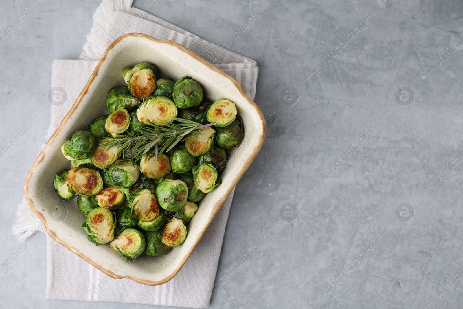 Photo of Delicious roasted Brussels sprouts and rosemary in baking dish on grey table, top view. Space for text