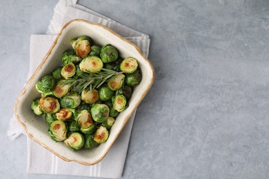 Photo of Delicious roasted Brussels sprouts and rosemary in baking dish on grey table, top view. Space for text