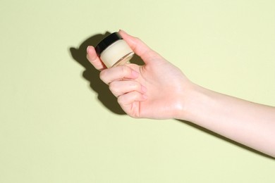 Woman holding jar of cream on green background, closeup