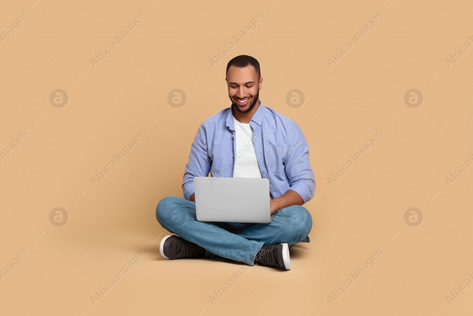 Photo of Smiling young man working with laptop on beige background