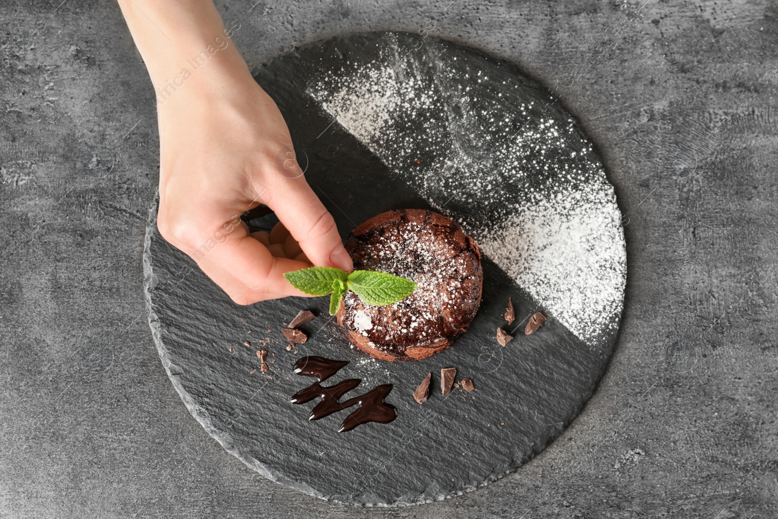 Photo of Chef decorating delicious fresh chocolate fondant with mint at table, top view. Lava cake recipe