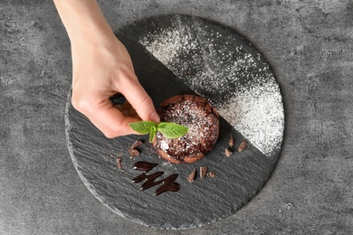 Photo of Chef decorating delicious fresh chocolate fondant with mint at table, top view. Lava cake recipe