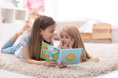 Cute little sisters reading book together at home