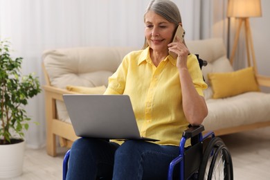 Photo of Woman in wheelchair talking on smartphone while using laptop at home