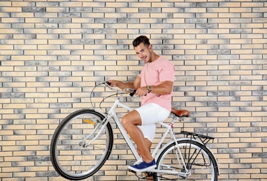 Photo of Handsome young hipster man with bicycle on brick wall background