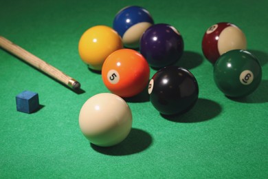 Photo of Many colorful billiard balls, cue and chalk on green table