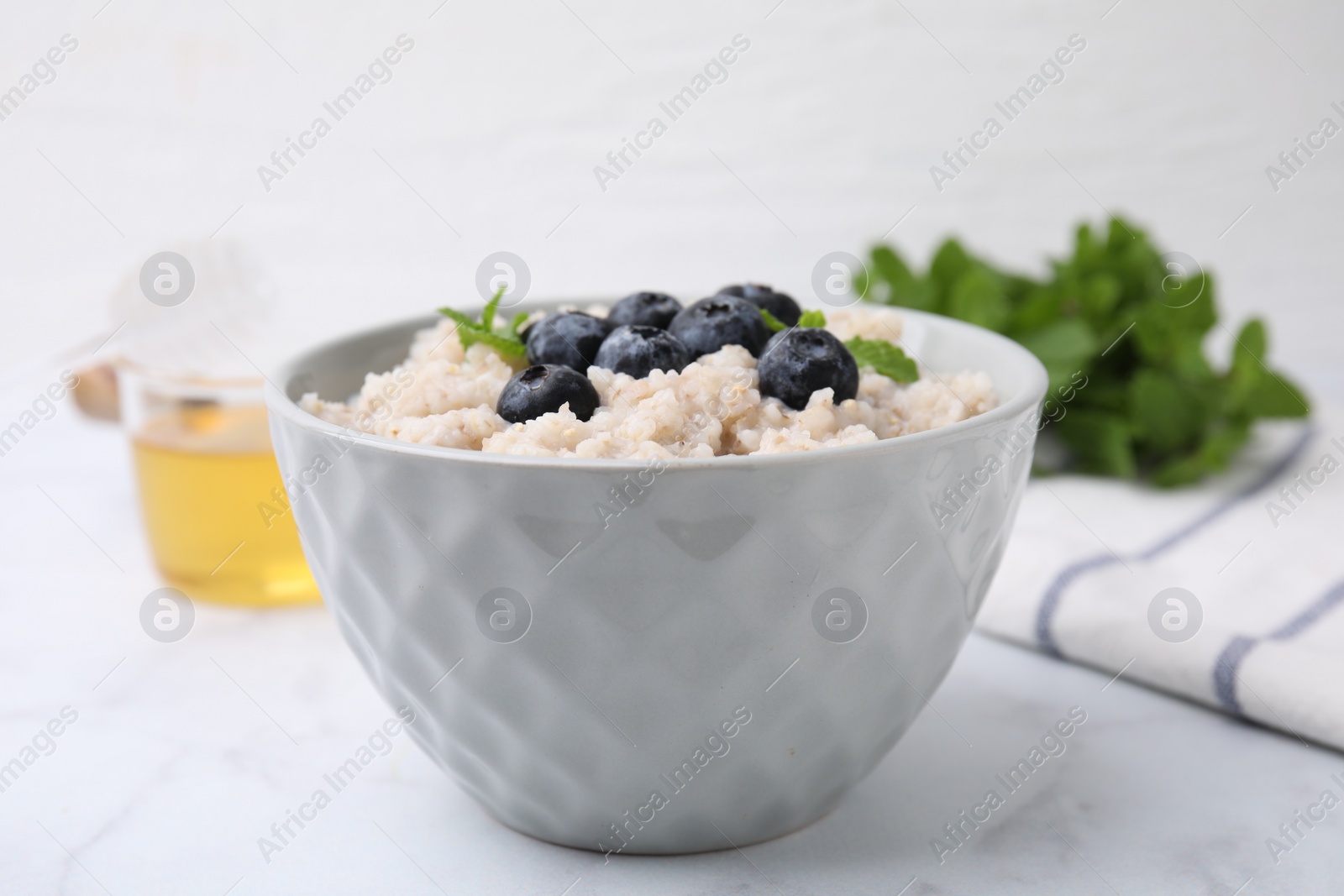 Photo of Delicious barley porridge with blueberries and mint in bowl on white marble table, closeup