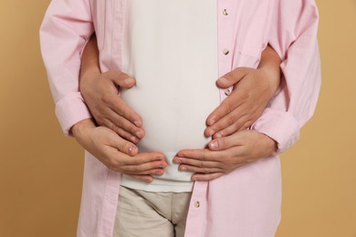 Photo of Man hugging his pregnant wife on light brown background, closeup