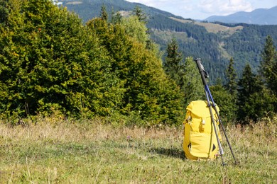 Photo of Yellow backpack and trekking poles outdoors on sunny day. Mountain tourism