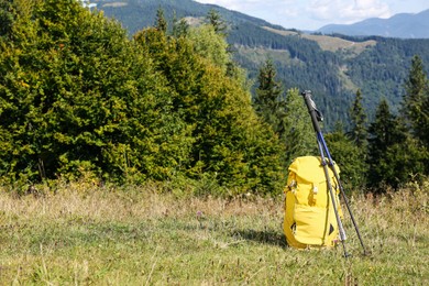 Yellow backpack and trekking poles outdoors on sunny day. Mountain tourism