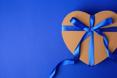 Photo of Beautiful heart shaped gift box with bow on blue background, top view. Space for text