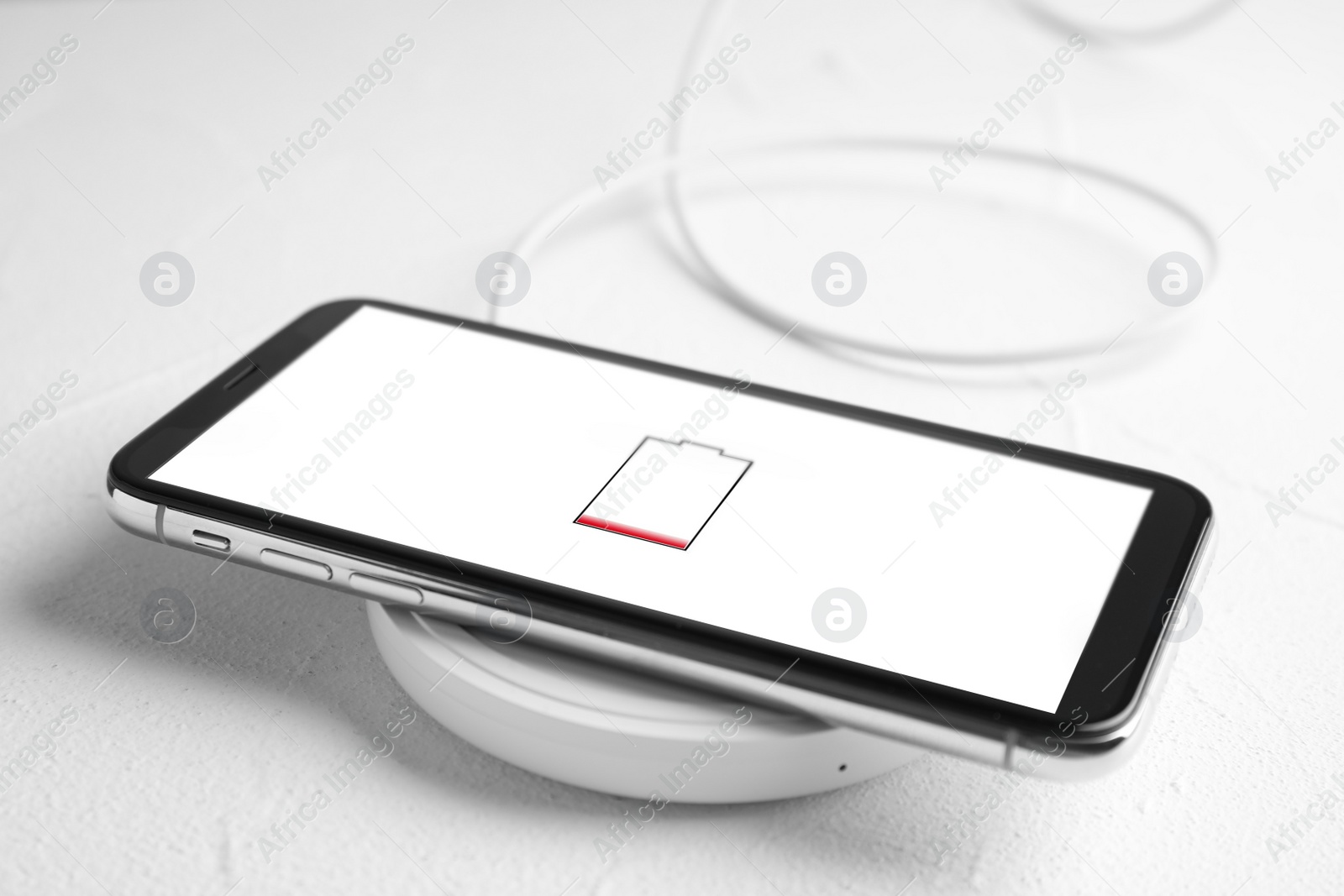 Photo of Mobile phone charging with wireless pad on white stone table, closeup