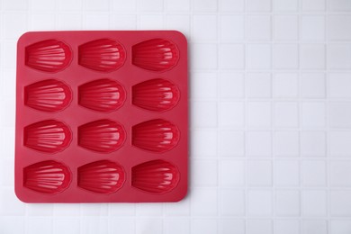 Red baking mold for madeleine cookies on white tiled table, top view. Space for text