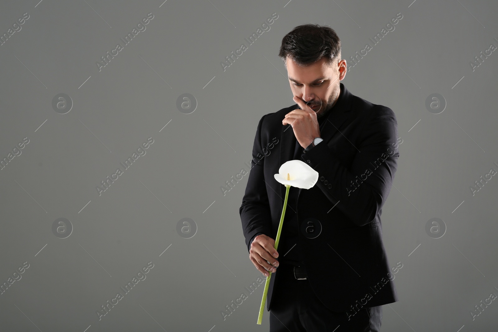 Photo of Sad man with calla lily flower mourning on grey background, space for text. Funeral ceremony