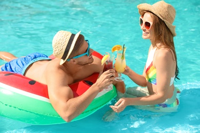 Young couple with cocktails in pool on sunny day