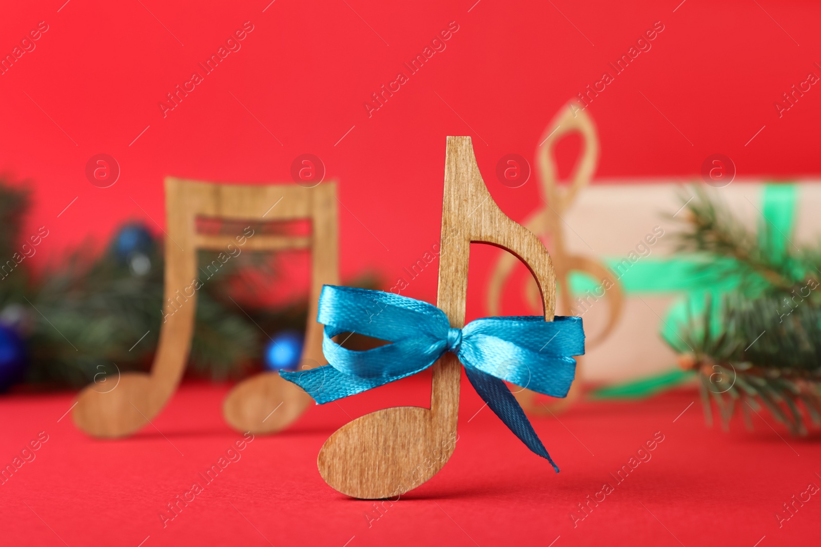 Photo of Wooden music note with blue bow on red background, closeup. Christmas celebration