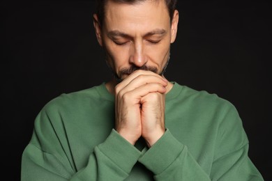 Photo of Man with clasped hands praying on black background, closeup