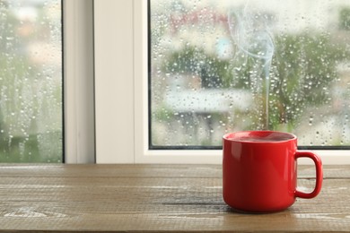 Photo of Cup of hot drink near window on rainy day. Space for text