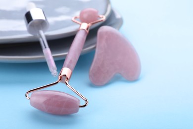 Photo of Rose quartz gua sha tool , facial roller and dropper on light blue background, closeup. Space for text
