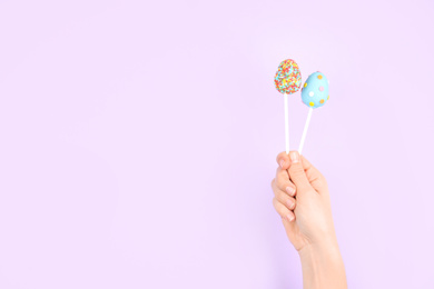 Photo of Closeup view of woman with delicious cake pops on light pink background, space for text. Easter holiday