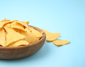 Photo of Wooden bowl of tasty Mexican nachos chips on light blue background. Space for text
